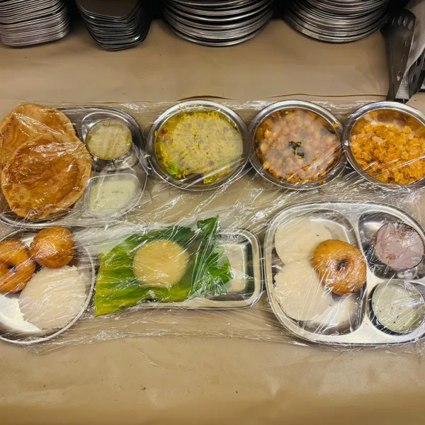Steel plates of poori, idli, vada, sheera on banana leaf and chutneys
